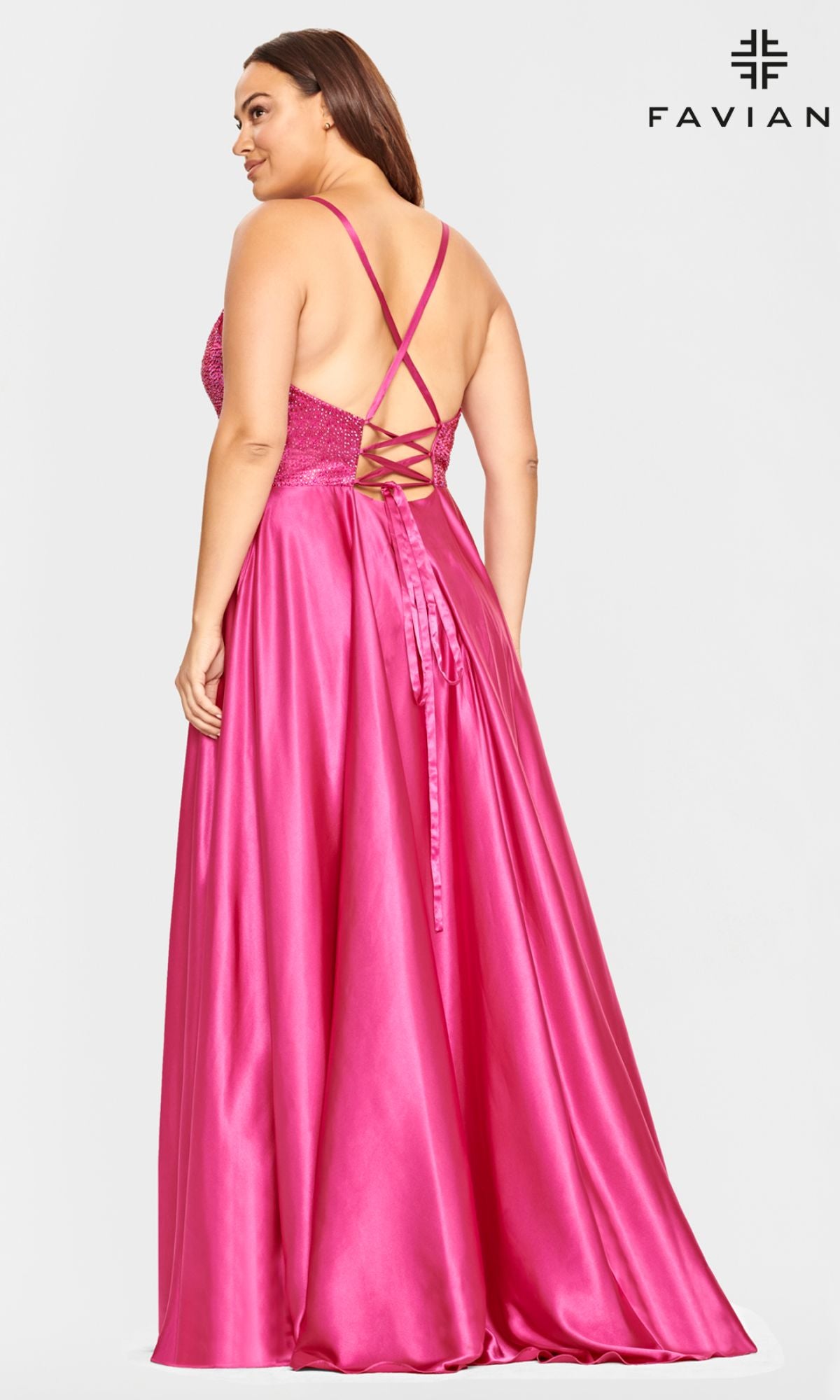 A woman stands facing away in a pink satin Faviana Plus-Size Prom Dress, featuring a sleeveless, floor-length design and strappy lace-up back—ideal for formal occasions.